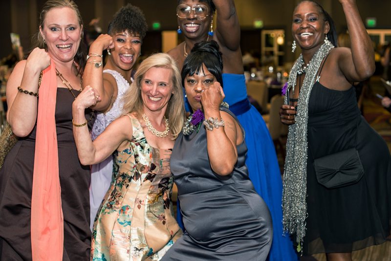 Women's Empowerment's Executive Director, Lisa, posing with a group of five Women's Empowerment graduates, at a Women's Empowerment Gala, all dressed in gowns.