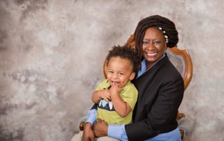 Women's Empowerment graduate, Robin, in professional clothes, holding her son, both smiling at the camera in front of a backdrop