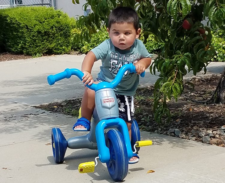 A young boy riding a tricycle in the backyard of Women's Empowerment
