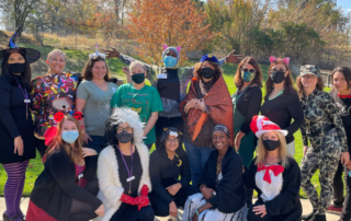 Session 85 students with staff, dressed in festive costumes on Halloween, in the backyard of Women's Empowerment.