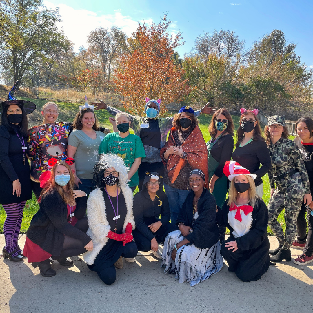 Session 85 students with staff, dressed in festive costumes on Halloween, in the backyard of Women's Empowerment.