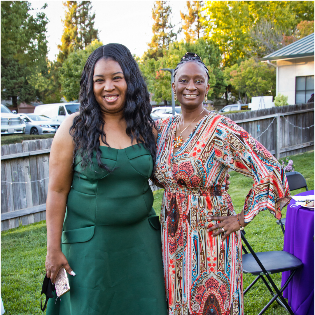 Two Women's Empowerment graduates, Natoshi and Robin, smiling and posing for the camera, in the backyard of Women's Empowerment, during the 2021 Grad Gala Celebration.